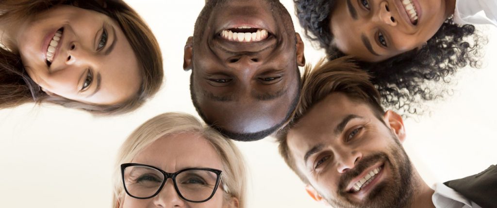 Low angle shot of smiling diverse office employee looking at camera hugging happy with career choice or company, excited multiethnic work team standing in circle engaged in team building activity