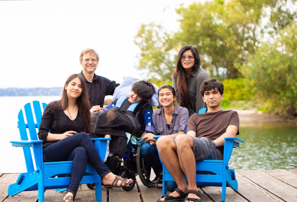 Familia, incluido el niño en silla de ruedas sentados juntos al aire libre en verano